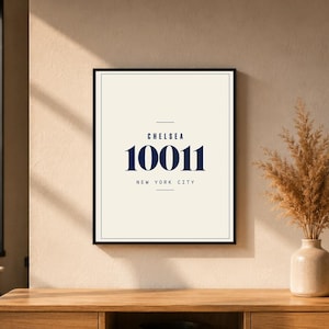 Può includere: Stampa artistica incorniciata con il testo "CHELSEA 10011 NEW YORK CITY" in blu navy su sfondo bianco sporco. La stampa è in una cornice nera. Un vaso con fiori secchi è a destra, su una superficie di legno.