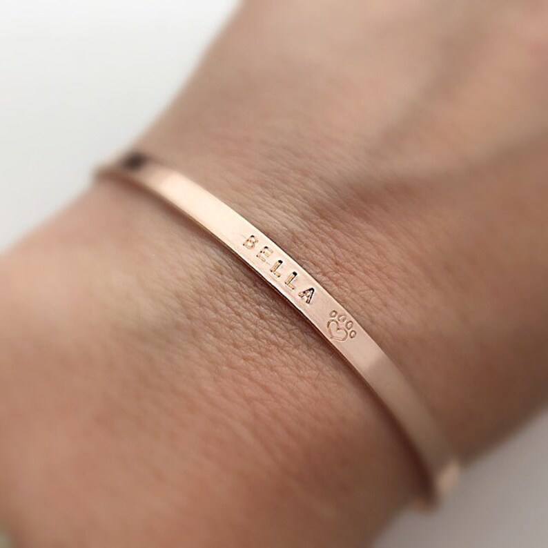 A cuff bracelet engraved with a name and a paw print on it.