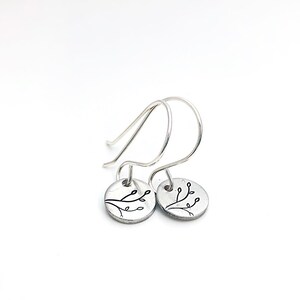 May include: Silver earrings with a delicate branch design. The earrings are small and have a simple, minimalist style.