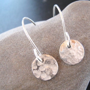 May include: A pair of silver dangle earrings with hammered round disc charms. The earrings have a simple, minimalist design.