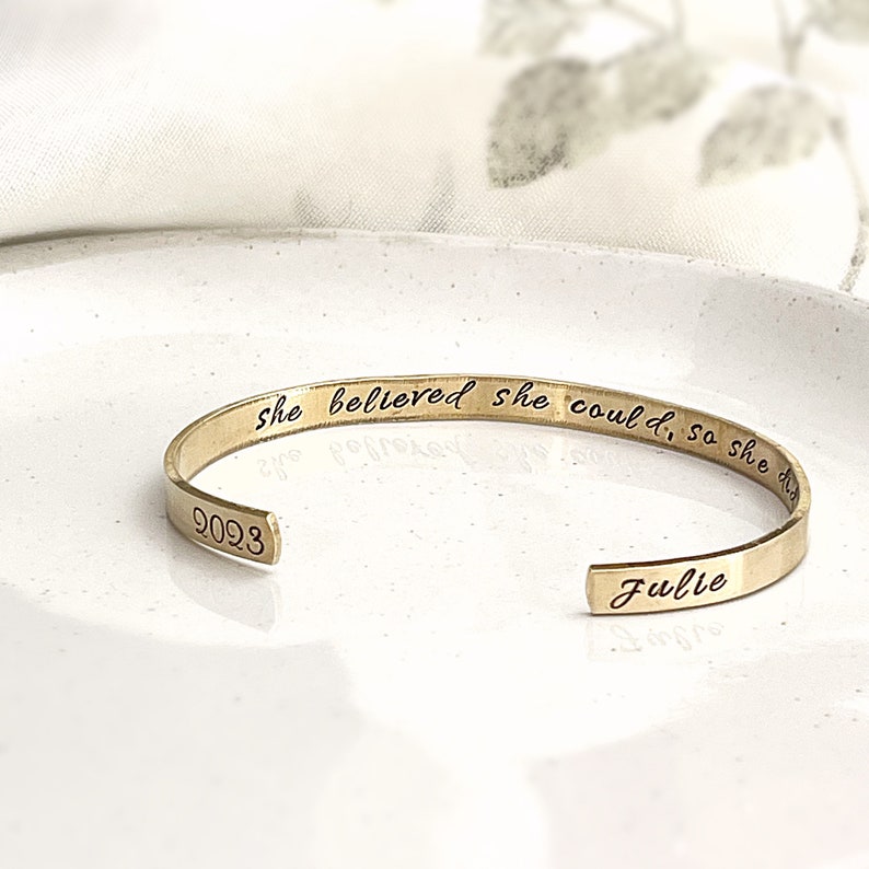 May include: Gold-toned bangle bracelet with the inscription "She believed she could, so she did." and the name "Julie" engraved on the other side. The bracelet also has the number "9023" engraved on the inside.