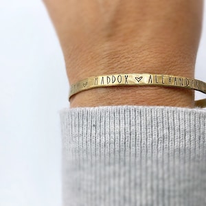 May include: A gold-toned metal bracelet with the inscription "Maddox ♥ Alexander" engraved on it.