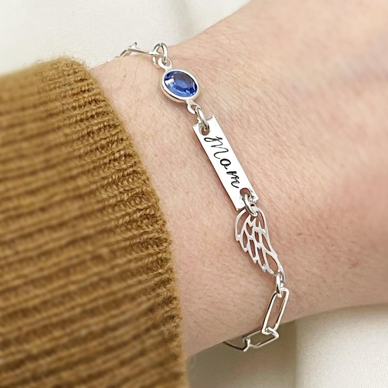 Op de afbeelding: Zilveren armband met een blauwe edelsteen, een bedel met de gravure "mam" en een vleugelbedel.