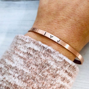 May include: A rose gold cuff bracelet with the initials "B" and "J" separated by a heart symbol.