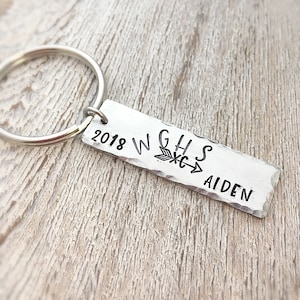 May include: Silver keychain with a rectangular tag that says "2018 WGHS" with an arrow pointing to the right and "AIDEN" below.