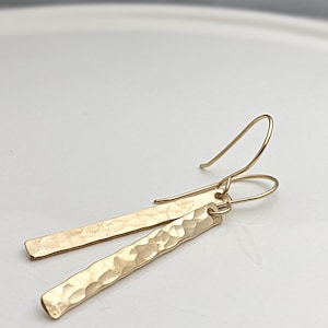 May include: A pair of gold hammered bar earrings with a simple hook closure.