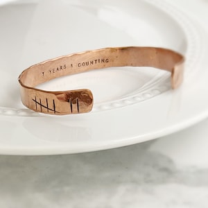 May include: A copper bracelet with the inscription "7 Years & Counting" and seven tally marks engraved on the band.
