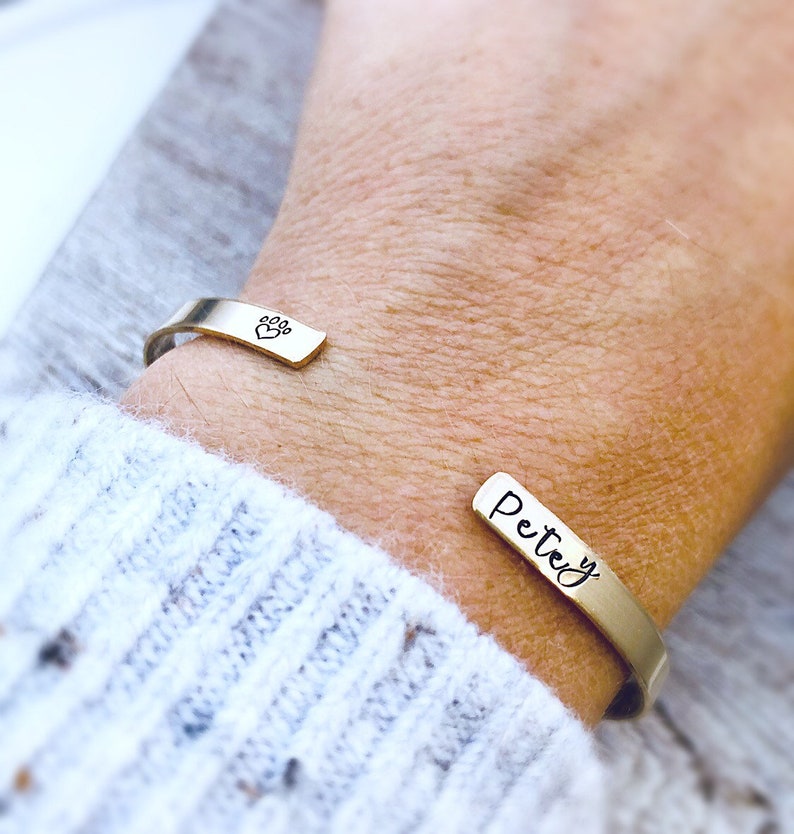May include: A gold-toned cuff bracelet with a paw print charm and the name "Petey" engraved on the other side.