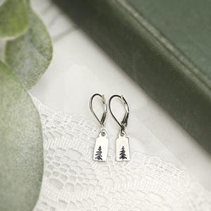 May include: A pair of silver dangle earrings with a small tree design on each charm.