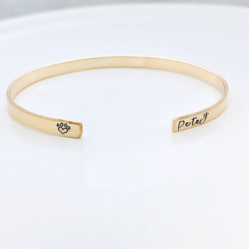 May include: Gold-toned bangle bracelet with a paw print and heart design on one side and the name "Petey" engraved on the other side.