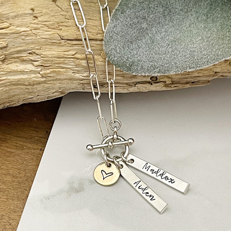 May include: Silver chain necklace with a toggle clasp and two personalized silver bar charms with the names Aiden and Maddox, and a gold heart charm.