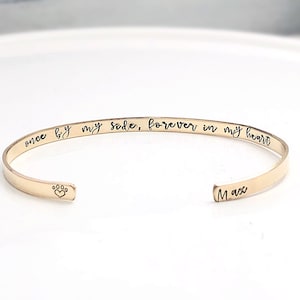 Pu&ograve; includere: Braccialetto rigido in oro con l'iscrizione "once by my side, forever in my heart" e un'impronta di zampa con un cuore all'interno. Il nome "Max" &egrave; inciso sull'altro lato.