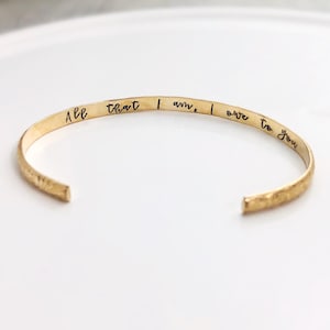 May include: Gold bangle bracelet with the inscription "All that I am, I owe to you".