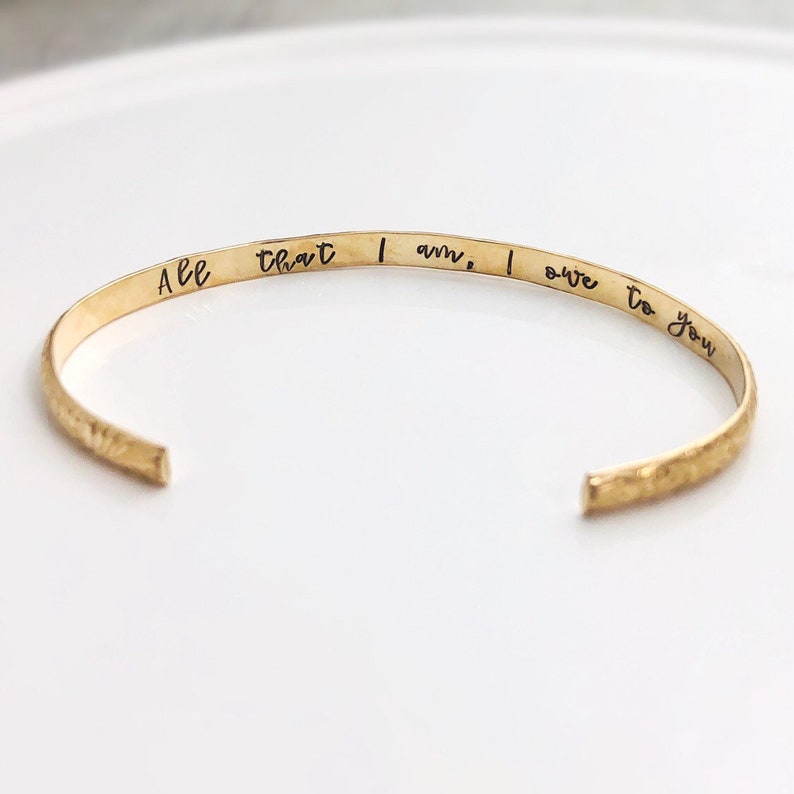 May include: Gold bangle bracelet with the inscription "All that I am, I owe to you".