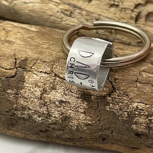 Peut inclure: Porte-clés en argent avec une étiquette ronde gravée du texte "DAD - CHRIS - BA" et un petit motif de croissant de lune.
