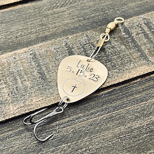 May include: Gold-colored fishing lure with a cross and a fish design. The lure is engraved with the text "Luke 5.15.23".