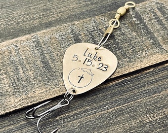 May include: Gold-coloured fishing lure with a cross and a fish design. The lure is engraved with the text "Luke 5.15.23".