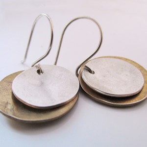 Peut inclure: Une paire de boucles d'oreilles en argent et en laiton au design simple et moderne. Chaque boucle d'oreille présente un disque rond en argent superposé à un disque rond en laiton plus grand.