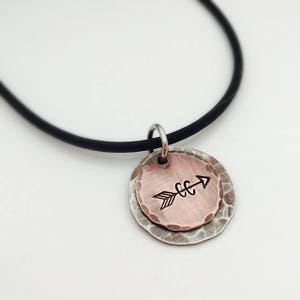 May include: A silver necklace with a black cord and a hammered copper pendant featuring an arrow design.