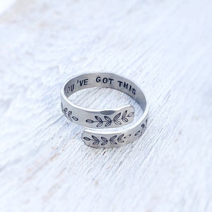 May include: A silver adjustable ring with the words "You've Got This" engraved on the band. The band is decorated with a repeating pattern of small leaves.