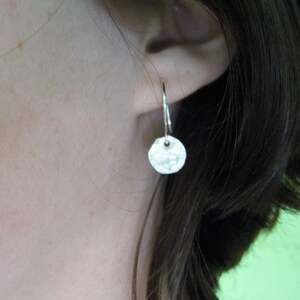 May include: Silver hoop earrings with a hammered, round disc pendant.