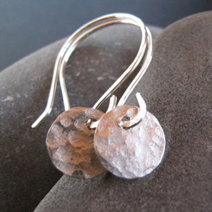 May include: A pair of silver earrings with hammered round discs hanging from simple wire loops.