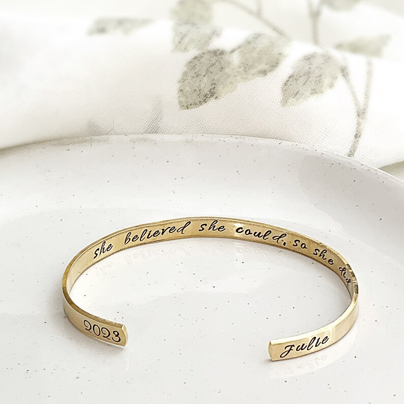 May include: Gold bangle bracelet with the inscription "She believed she could, so she did" and the name "Julie" engraved on the inside.