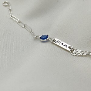 Op de afbeelding: Zilveren kettingarmband met een blauwe edelsteen, een bedel met de gravure "mam" en een vleugelbedel.