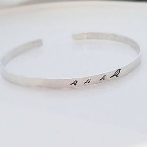 May include: A silver bangle bracelet with a row of five small bird silhouettes engraved on the front.