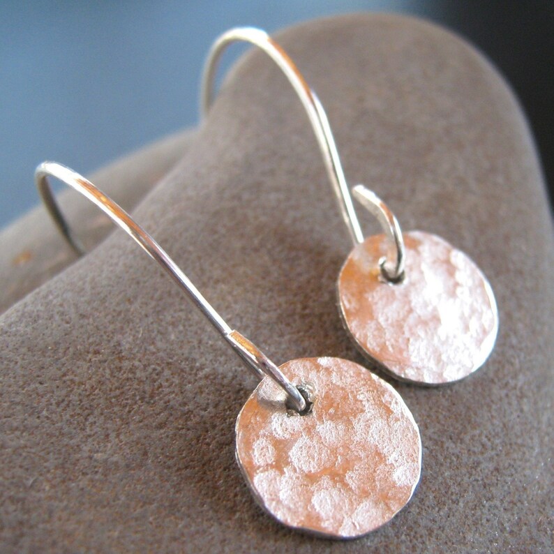 May include: A pair of silver dangle earrings with hammered round disc charms. The earrings have a simple, minimalist design.