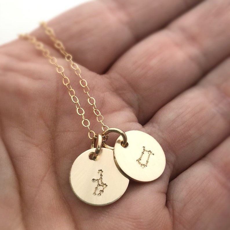 May include: Gold necklace with two round pendants featuring the constellation designs for Gemini and Virgo.