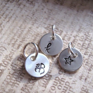May include: Three silver charms with different designs. The first charm has the letter "K" engraved on it. The second charm has a star engraved on it. The third charm has the Om symbol engraved on it.