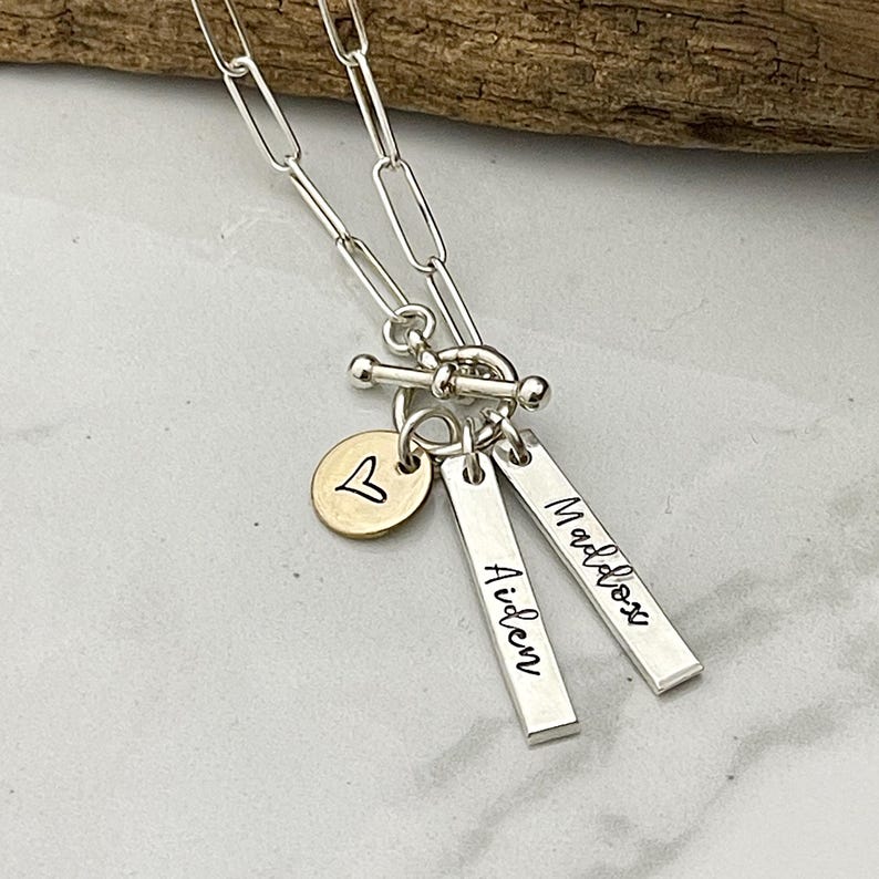 May include: Silver necklace with a heart charm and two personalized bar charms with the names "Maddox" and "Aiden".