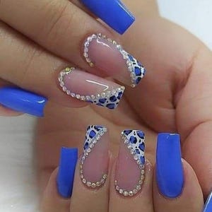 Puede incluir: Una mano con uñas acrílicas largas, azules y en forma de ataúd. Algunas uñas presentan una base transparente con un diseño de estampado de leopardo blanco y azul y detalles de pedrería. Las uñas son de un vibrante color azul cobalto.