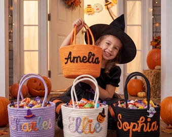 May include: Four round rope baskets for Halloween sweets, each featuring a personalised name embroidered on the front. The baskets are orange, lavender, white, and black, decorated with small felt icons like a witch hat, pumpkin, and ghost.