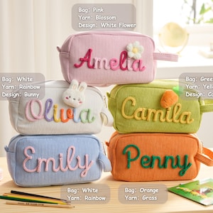 May include: Five rectangular corduroy pencil cases in pink, white, green, blue, and orange. Each case features a personalized name embroidered in yarn with decorative accents: a white flower, a bunny, a carrot, and plain lettering.