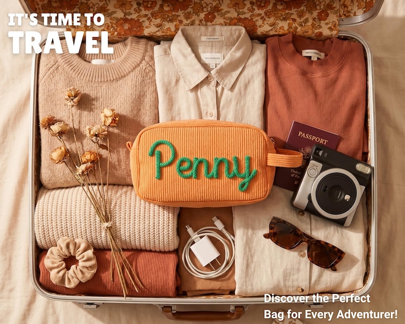 May include: A suitcase packed with a beige sweater, a cream button-down shirt, a rust-colored top, a beige scrunchie, a white charging cable, a passport, a camera, sunglasses, and an orange corduroy pouch with the green embroidered name Penny.