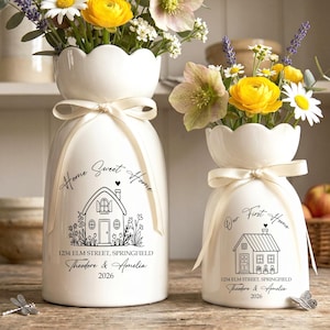 May include: Two white ceramic vases with scalloped rims and cream-coloured ribbons. The larger vase features the text Home Sweet Home, 1234 Elm Street, Springfield, Theodore & Amelia, 2026. The smaller vase features Our First Home, 1234 Elm Street, Springfield, Theodore & Amelia, 2026.