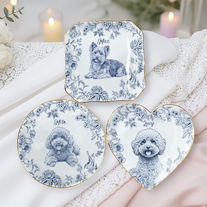 May include: Three decorative plates with blue floral designs and gold rims. Each plate features a different dog breed illustration and a name: Max, Mila, and Lucy. The plates are in square, round, and heart shapes.