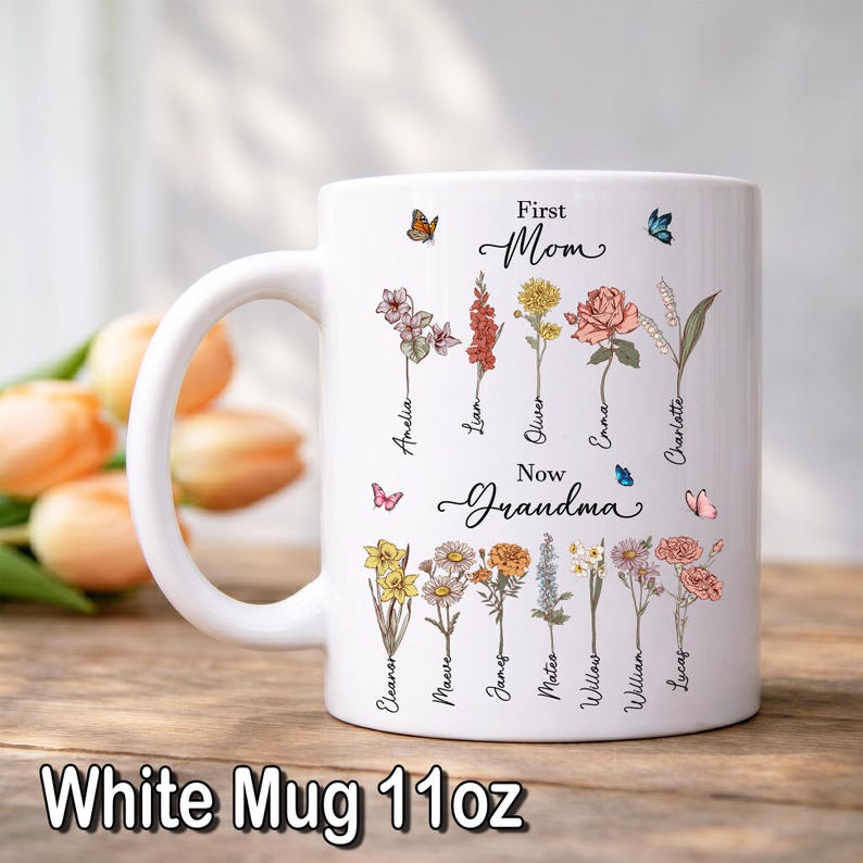 May include: White 11oz mug with floral illustrations and the text "First Mom Now Grandma." The mug features names like Amelia, Liam, and Emma, with butterflies. The bottom of the mug reads "White Mug 11oz."