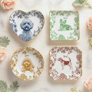 May include: Four decorative ceramic dishes with gold rims, each featuring a different dog breed illustration and name. The shapes include a heart, square, circle, and a square with curved edges. Floral patterns surround the dog portraits.