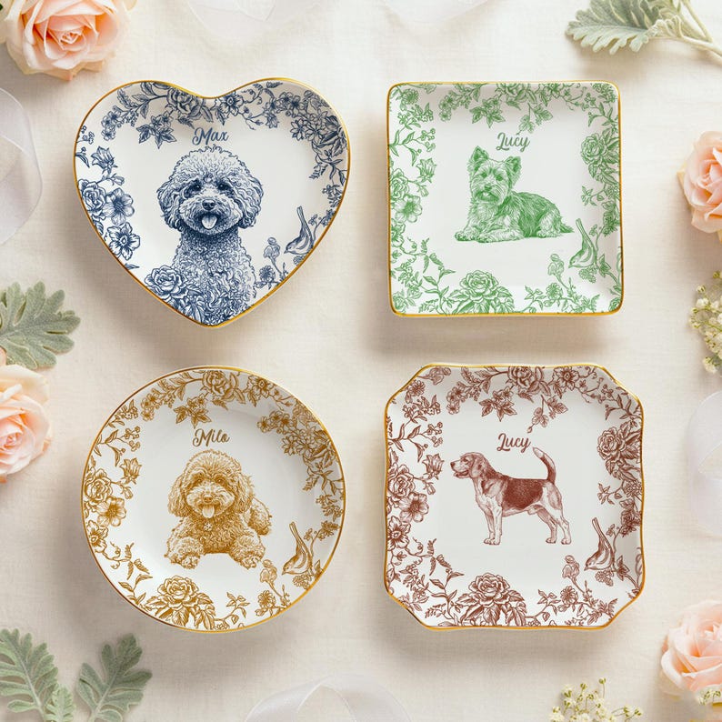 May include: Four decorative ceramic dishes with gold rims, each featuring a different dog breed illustration and name. The shapes include a heart, square, circle, and a square with curved edges. Floral patterns surround the dog portraits.