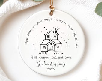 May include: A white ceramic ornament with a gold string for hanging. The ornament features a black line drawing of a house, the text "New Home - New Beginning - New Memories", the address "485 Coney Island Ave", the names "Sophia & Henry", and the year "2025".