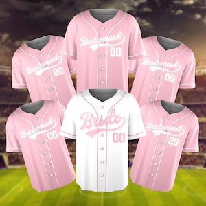 May include: Pink baseball jerseys with the word "Bridesmaid" in white script and the number "00". One white jersey with "Bride" in pink script and the number "00". All jerseys have a button-up front and white trim.