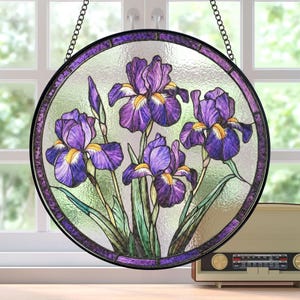 May include: A stained glass window panel depicting a cluster of purple irises with yellow centres. The panel is round and framed in black metal. It is hanging from a chain.