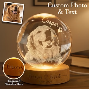 May include: A crystal ball lamp featuring a Golden Retriever dog, with the name "Cooper" and paw prints engraved on the glass. The lamp sits on a wooden base with the words "forever loved" and the years 2010-2026 engraved. The lamp is lit from within.