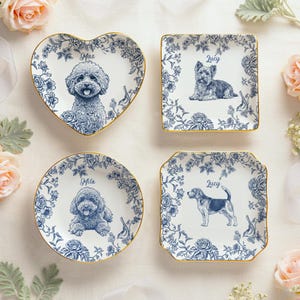 May include: Four decorative ceramic plates with blue floral designs and gold rims. Each plate features a different dog breed illustration and a name: Max, Lucy, Mila, and Lucy. The plates are in heart, square, and round shapes.