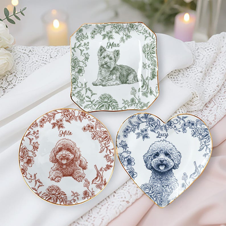 May include: Three decorative ceramic plates with dog portraits. One is square with a green floral border and a dog named Max. Another is round with a brown floral border and a dog named Mila. The third is heart-shaped with a blue floral border and a dog named Lucy.