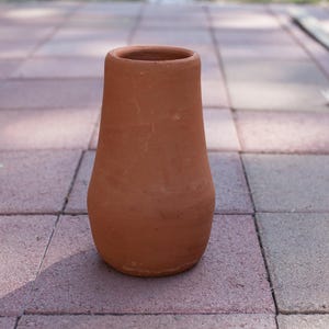 May include: A terracotta vase with a smooth, matte finish and a tapered cylindrical shape. The vessel features a wide, rounded base that narrows toward the top opening, showcasing a natural, earthy reddish-brown color throughout the exterior.