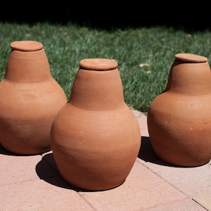 May include: Three terracotta-colored ceramic jars with lids. The jars are pear-shaped and have a smooth, slightly textured surface.